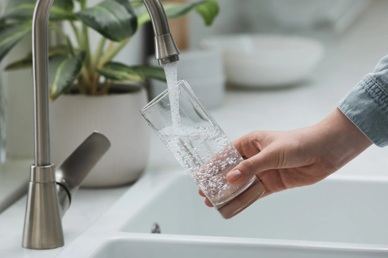 A hand filling a glass of water from a kitchen faucet