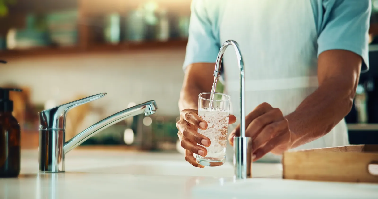 Hands filling a glass of water from a kitchen tap