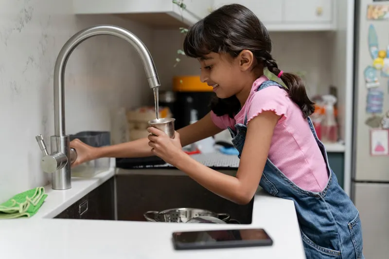 A girl filling a metal cup with water from a kitchen tap